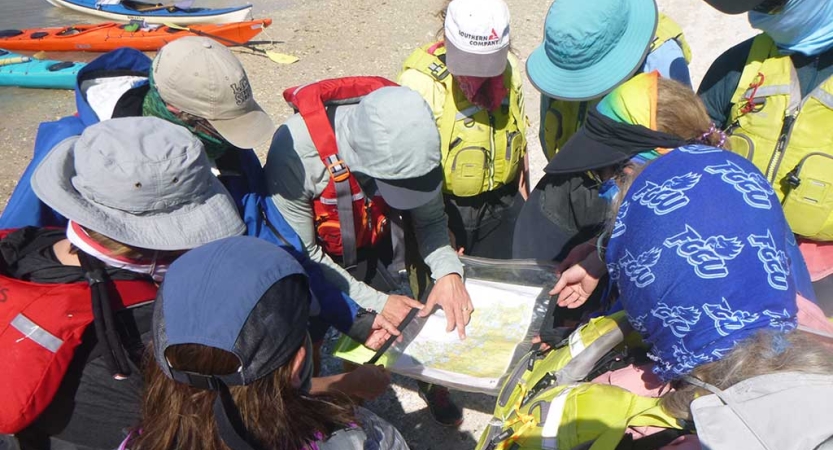 A group of people gather around a map on a sandy beach